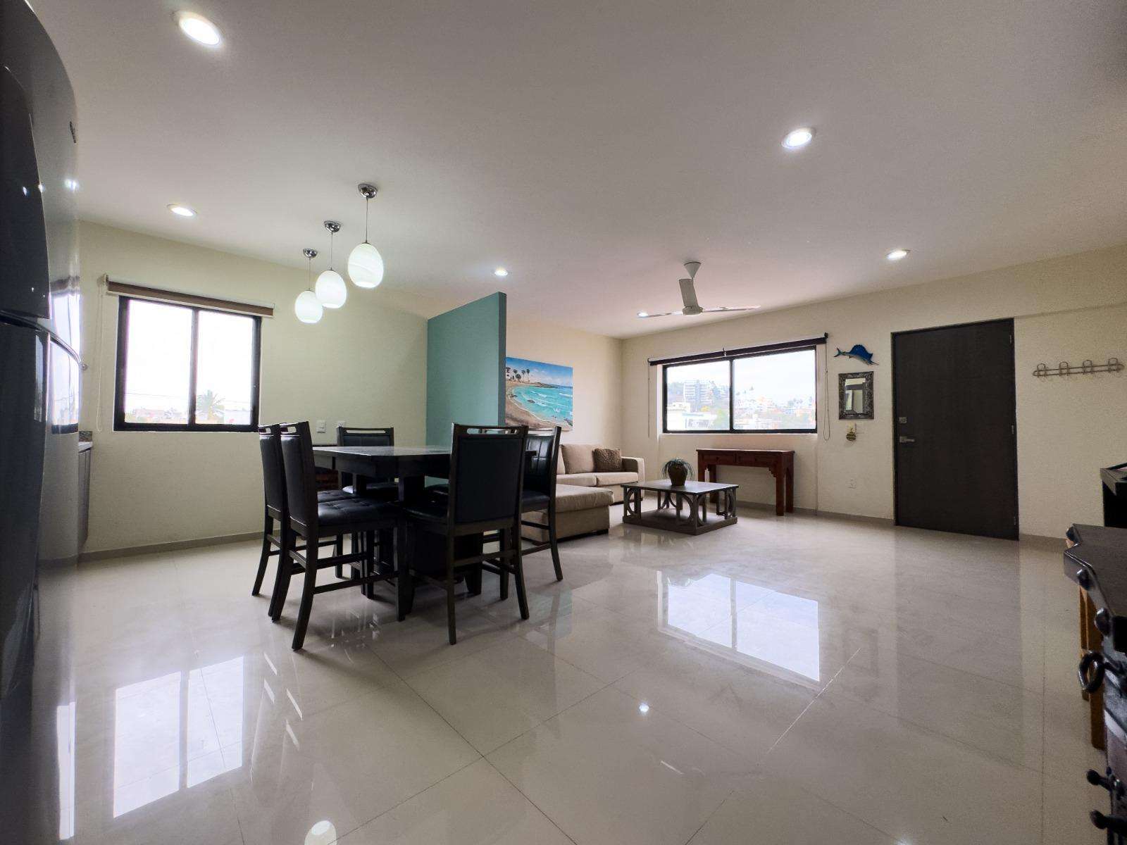 Open dining and living area with dark wood furniture, cream sofa, and large windows flooding light. - property