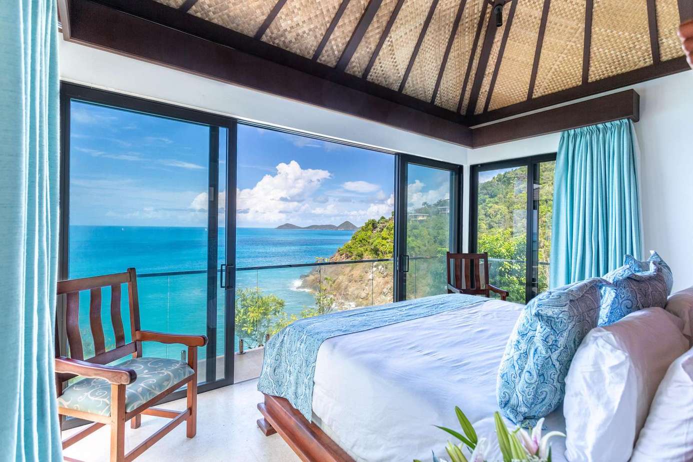 Oceanfront bedroom with panoramic glass walls and tropical views