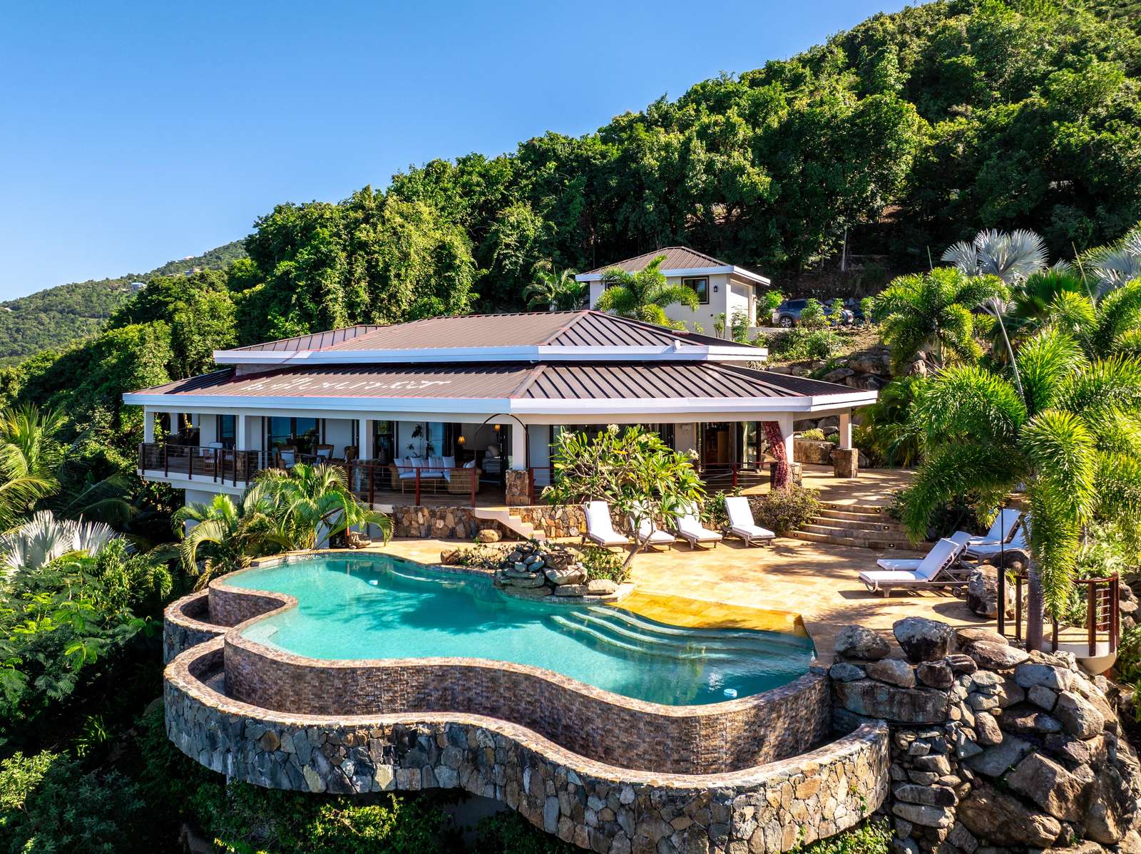 Sun-soaked patio with infinity pool and lush hillside views - property