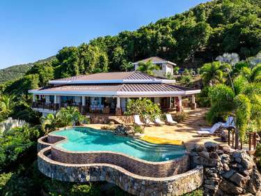 Sun-soaked patio with infinity pool and lush hillside views