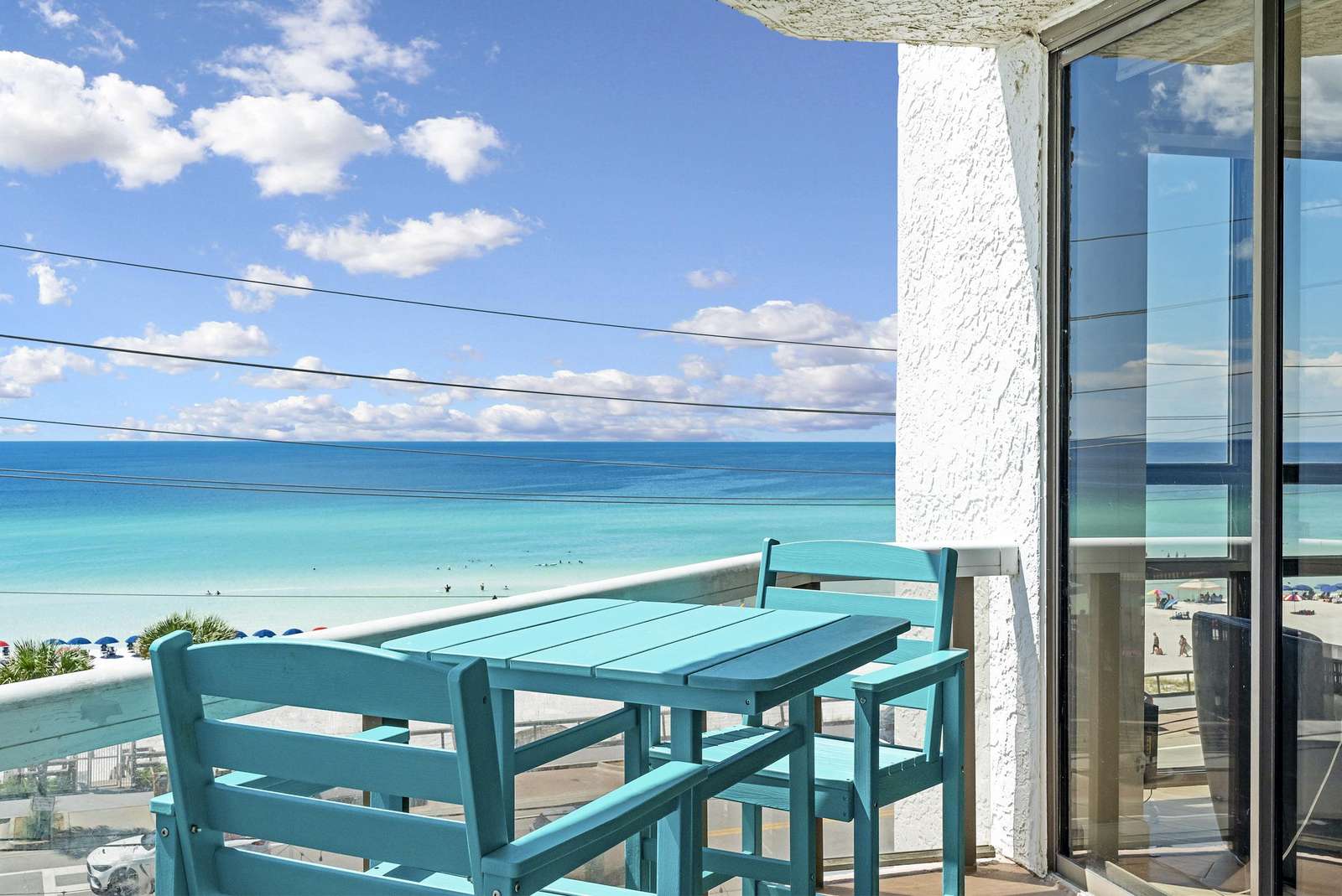 Turquoise wooden table and chairs sit on the balcony overlooking the beach and turquoise ocean waters. - property
