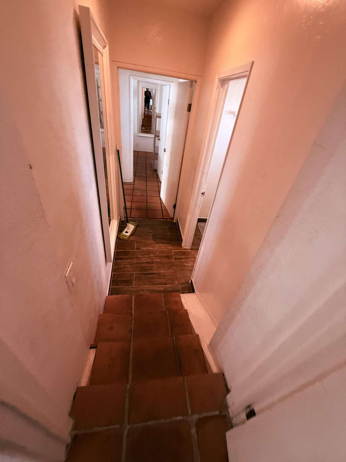 Upstairs terracotta stairs lead down to a hallway from back bedroom to front bedroom next to bathrooms.