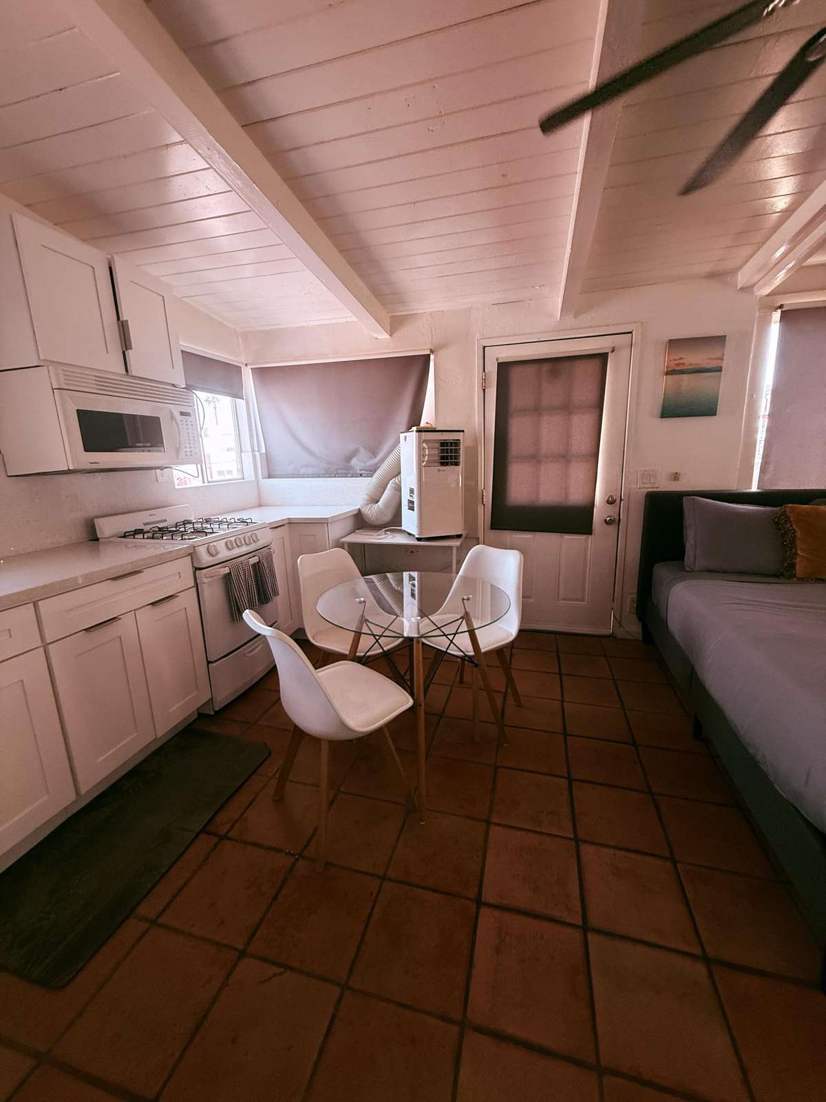 Kitchenette with white cabinetry, terracotta tile flooring, glass dining table in back bedroom with 2 queen beds.
