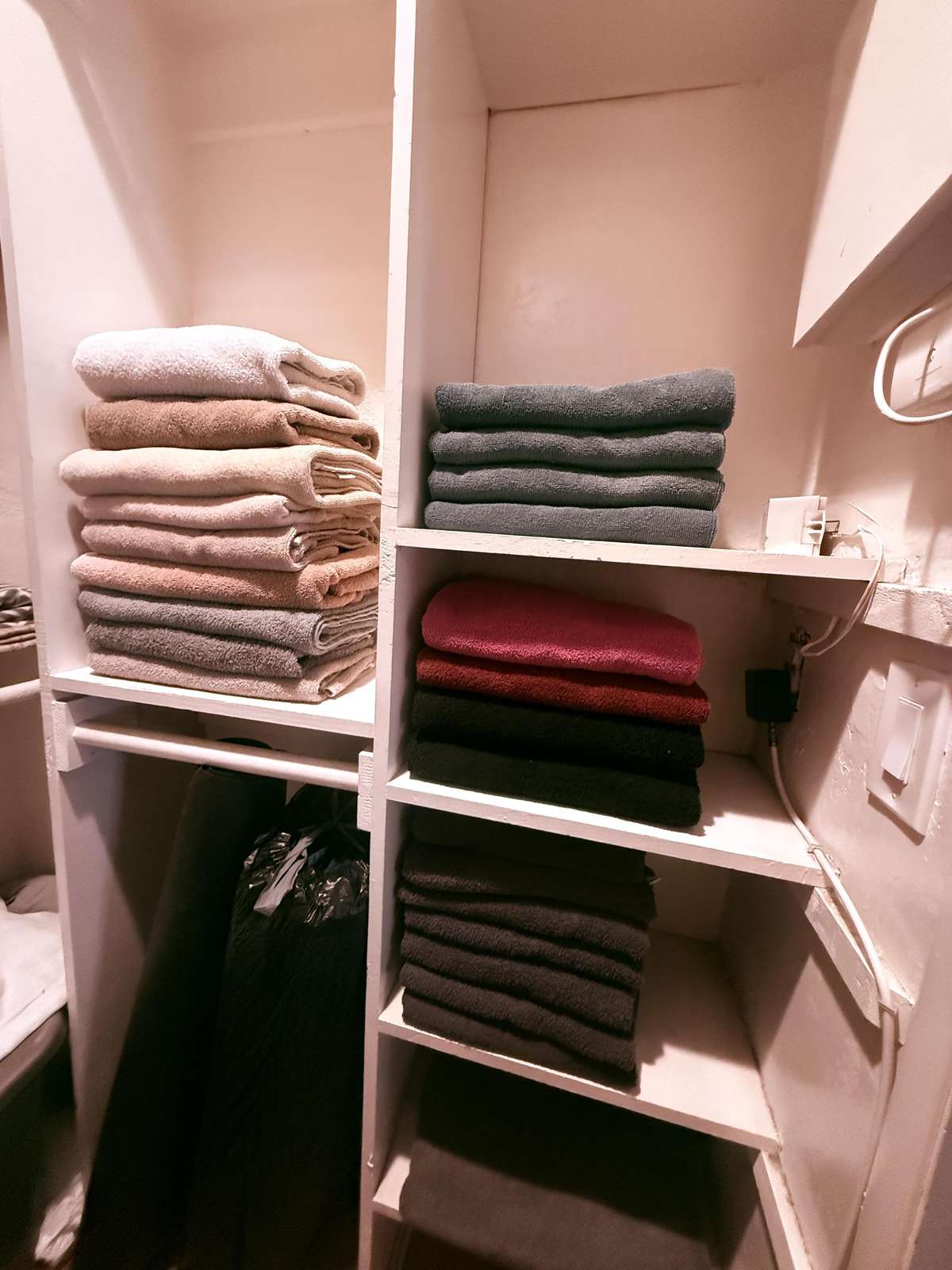 Closet shelves stocked with neatly folded towels in shades of gray, beige, and burgundy.