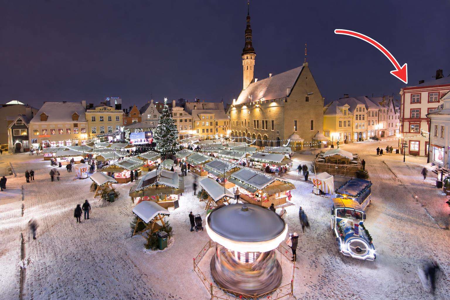 Night view of a festive market square with snow-covered stalls, a large decorated Christmas tree, and a spinning carousel. - property
