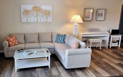Wohnzimmer mit Ecksofa, Klavier und Palmenbild