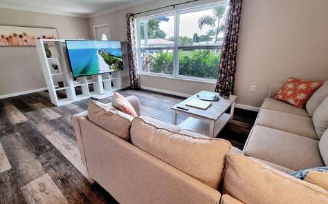 Wohnzimmer mit Ecksofa und Fernseher am Gartenfenster