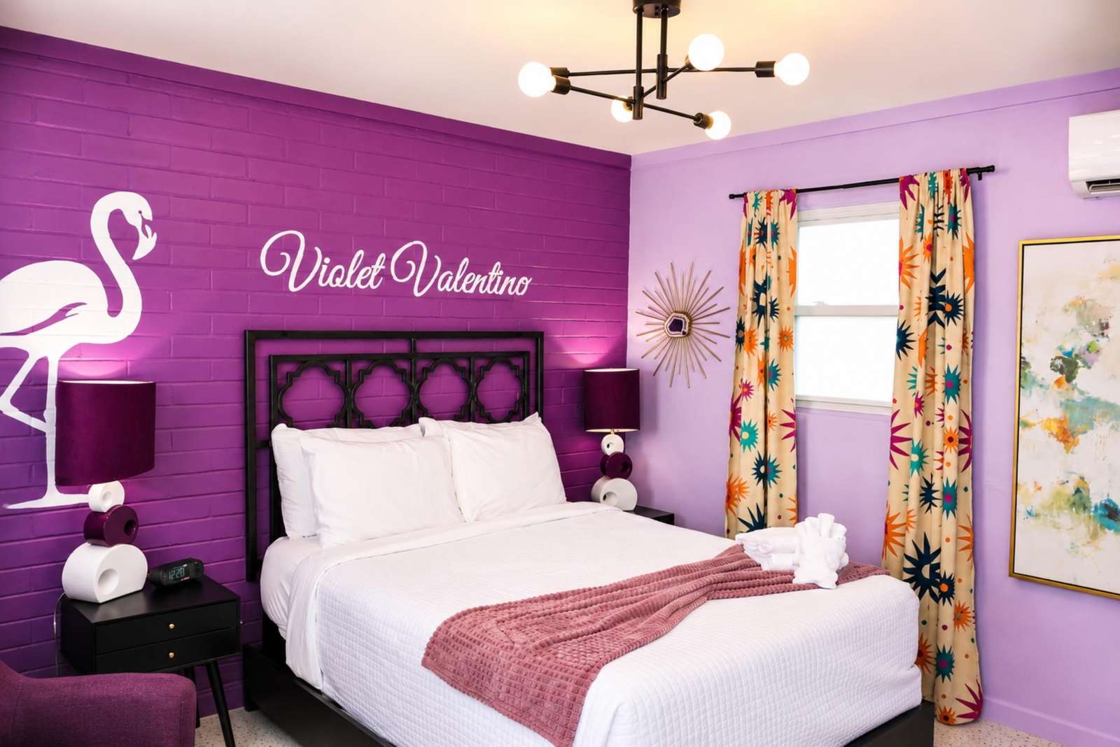 Purple brick accent wall with flamingo graphic anchors the bedroom, paired with patterned curtains and sculptural lamps. - property