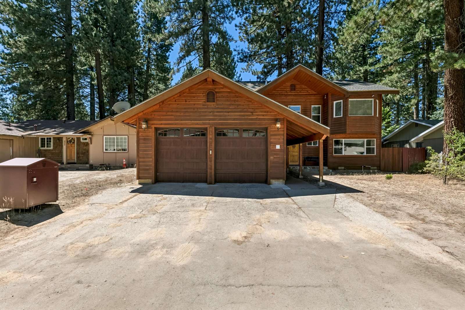 Exterior view of the wood-paneled house with a double garage and tall pine trees surrounding the property. - property