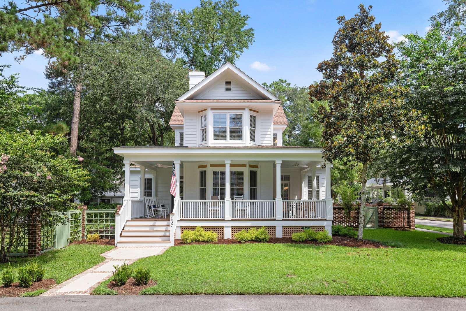 Traditional two-story house with white siding, wide porch with rocking chairs, and lush green lawn. - property