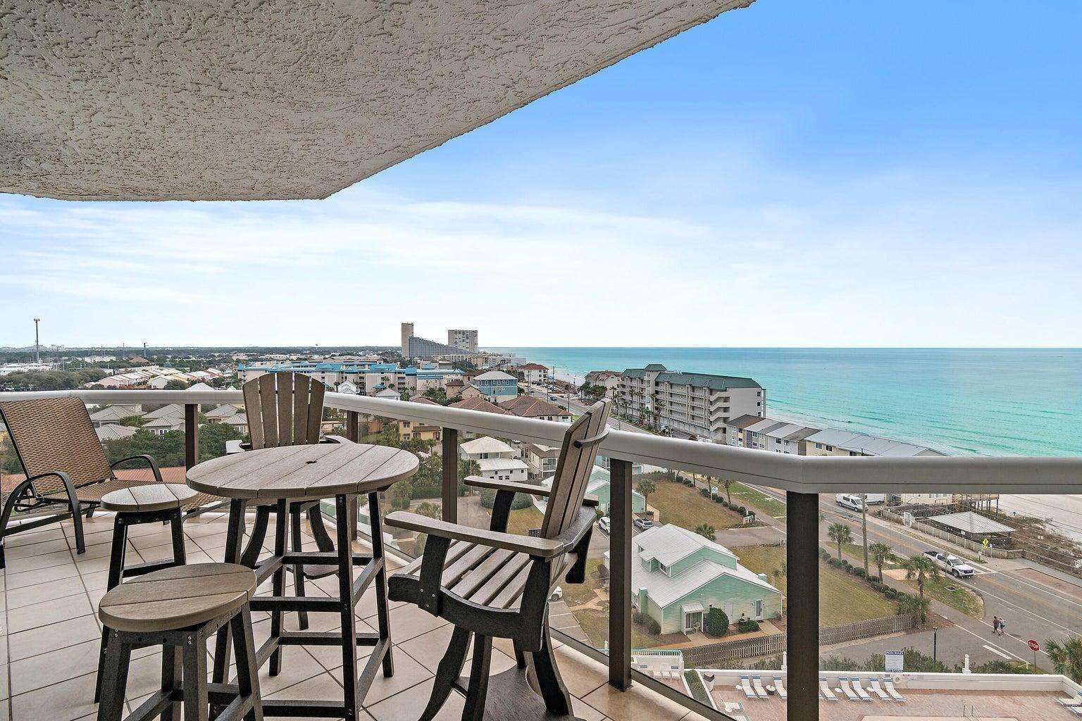 Outdoor balcony seating includes a round wooden table with stools and Adirondack chair beside glass railing. - property