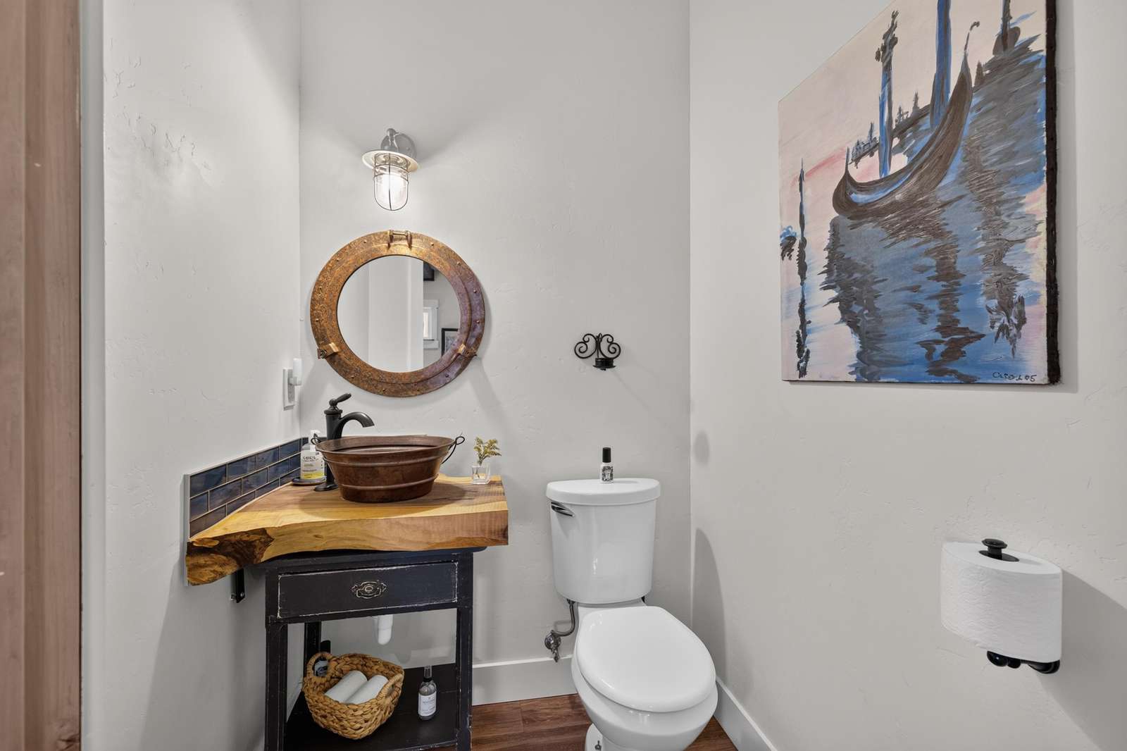 Half bathroom features a live-edge wood countertop with copper vessel sink and circular rustic mirror.