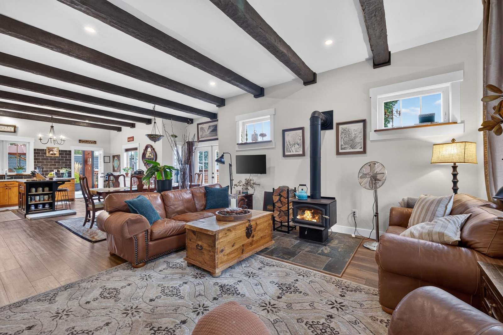 Leather sofas face a wood-burning stove set on slate tiles beneath dark ceiling beams in the open living area.