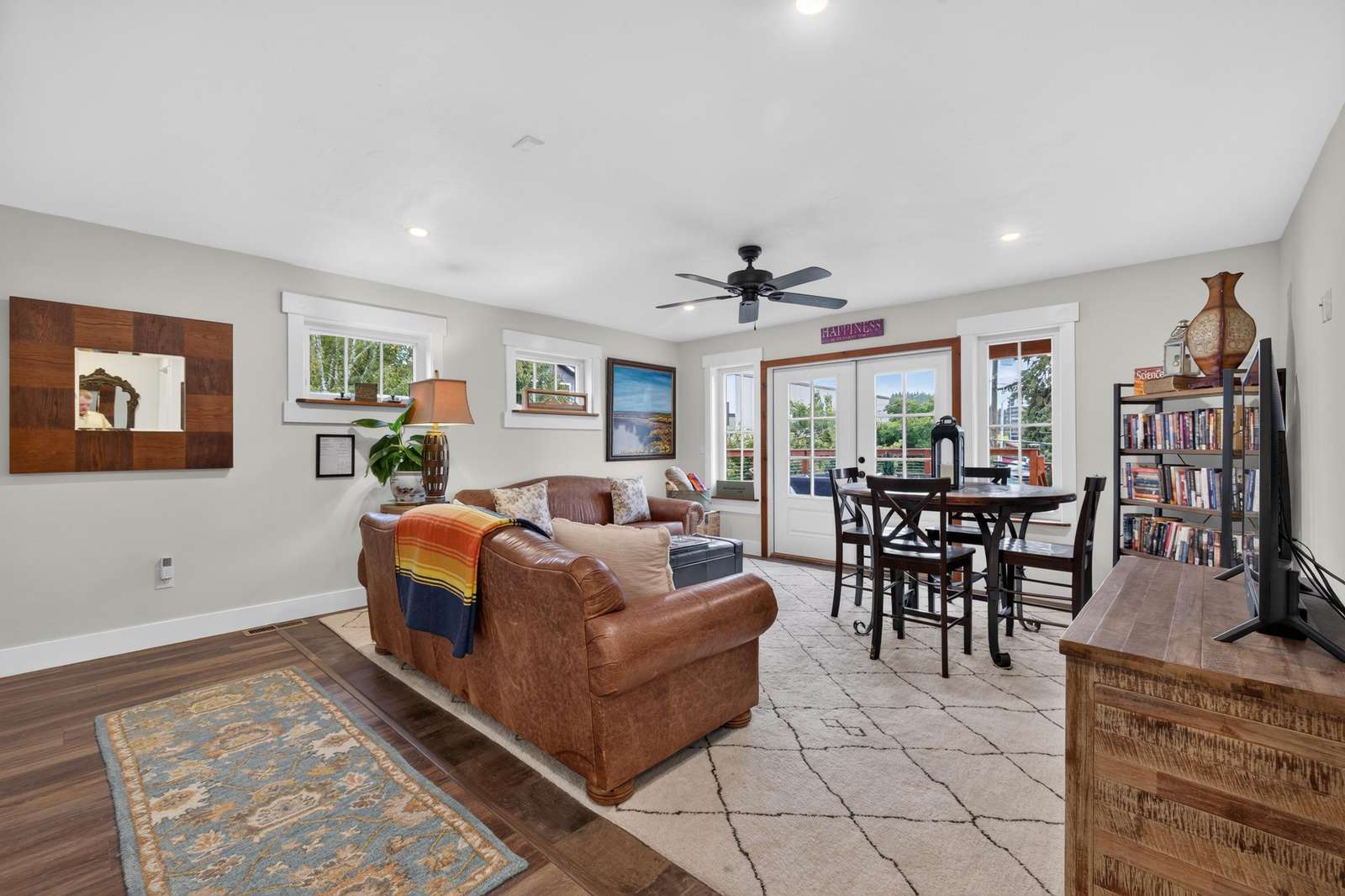 Living area features a leather sofa, patterned area rug, round dining table, and French doors opening to a balcony.