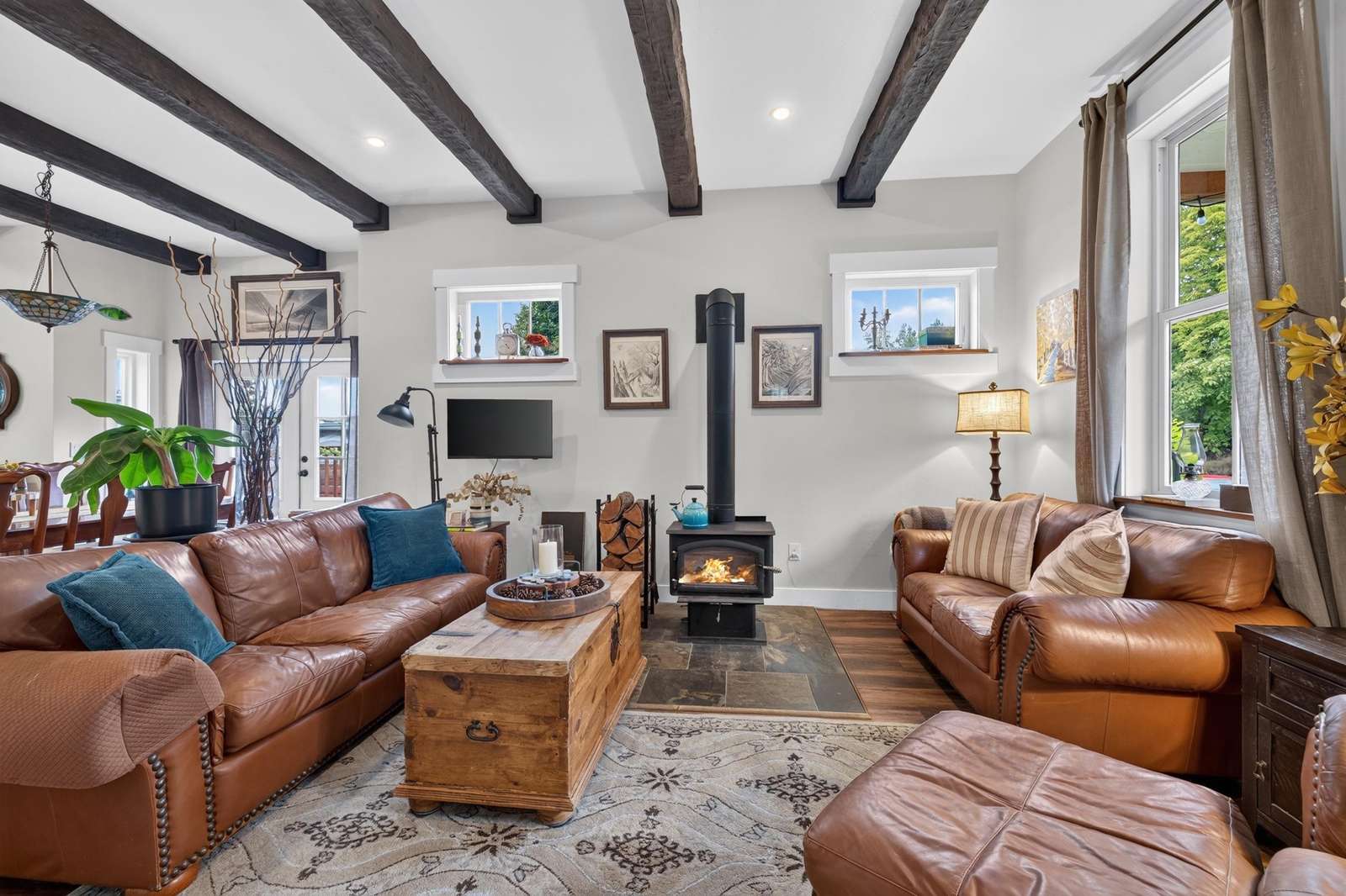 Living room with leather sofas, wood-burning stove on slate hearth, exposed beams, and natural light through windows.