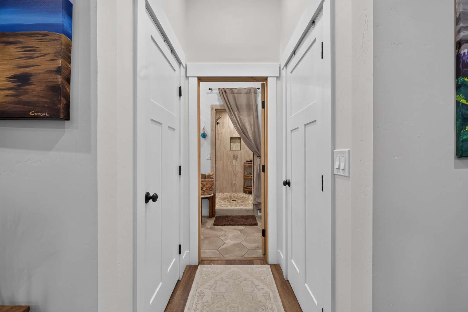 Hallway with white paneled doors, wood trim, and a view into a tiled walk-in shower behind a beige curtain.