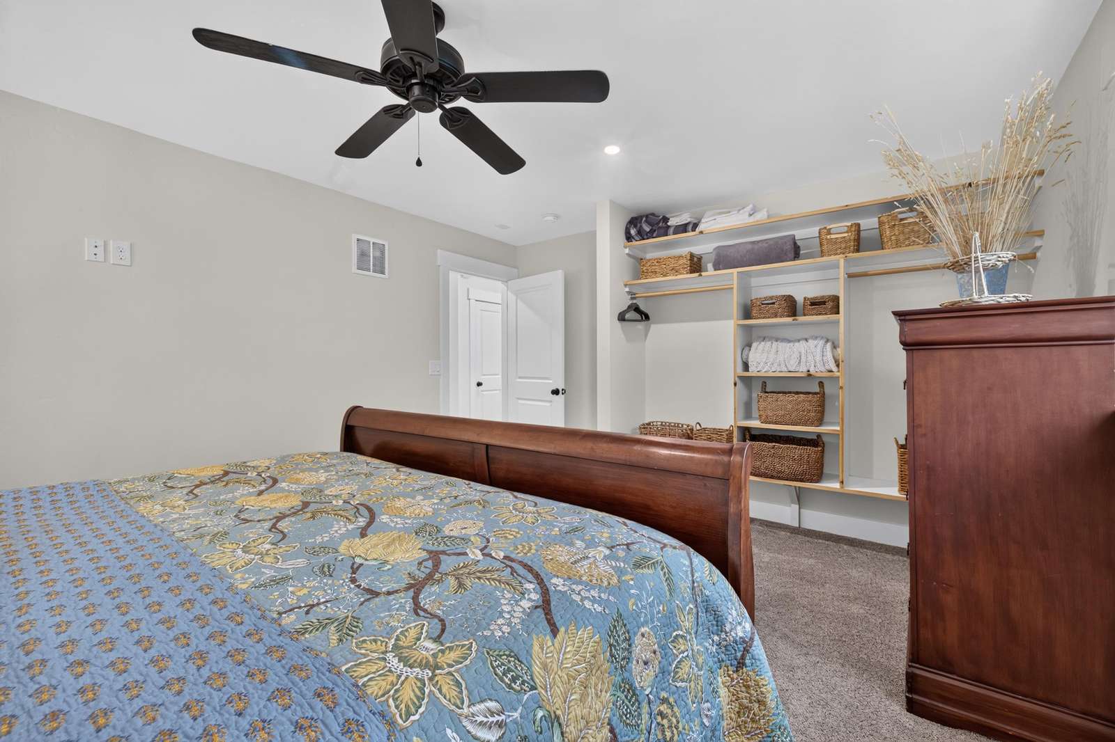 Bedroom features a dark wood sleigh bed, open shelving with woven baskets, and a ceiling fan overhead.
