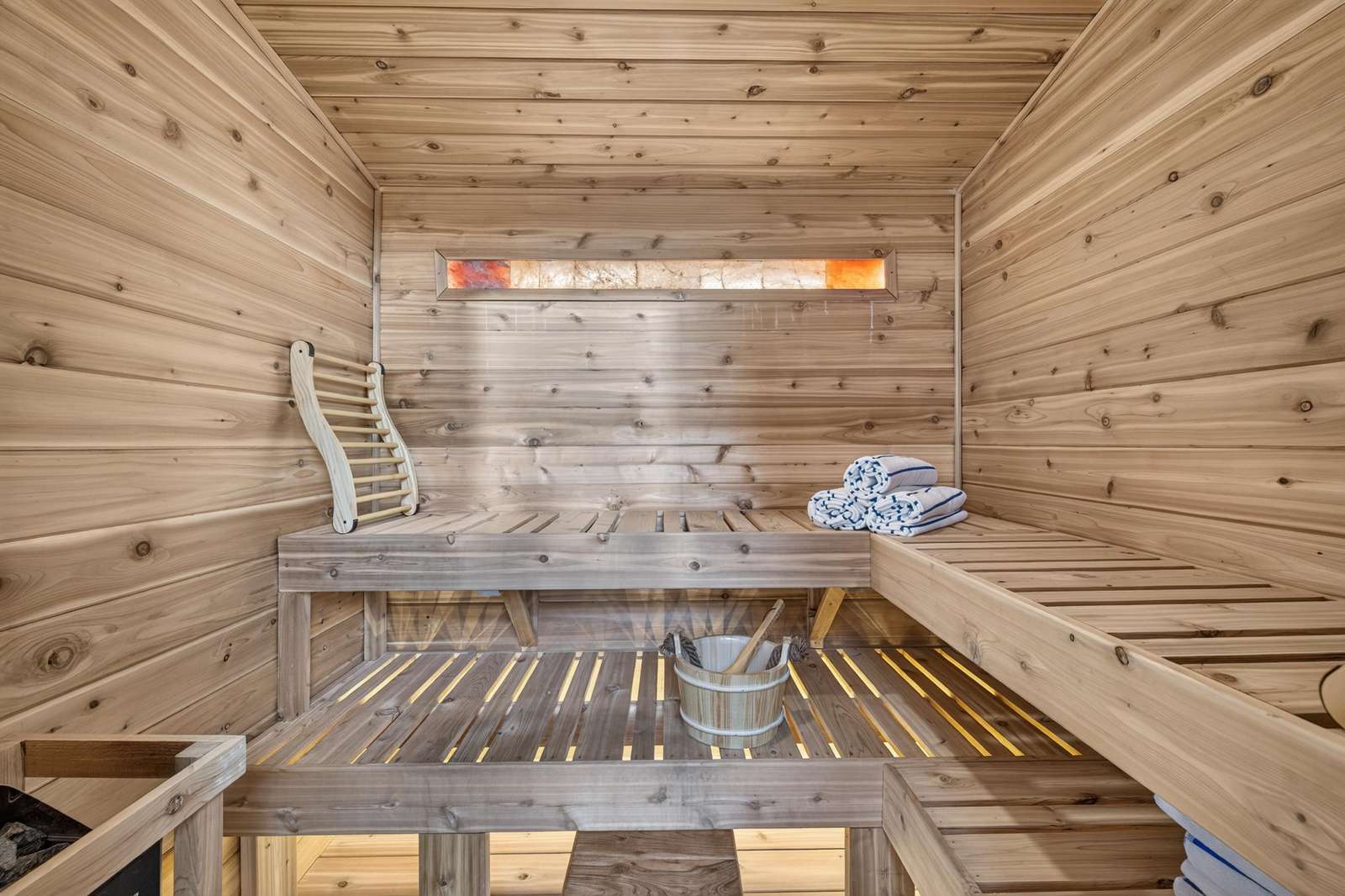 Light-toned cedar panels line the sauna interior, with slatted wooden benches and rolled white towels.