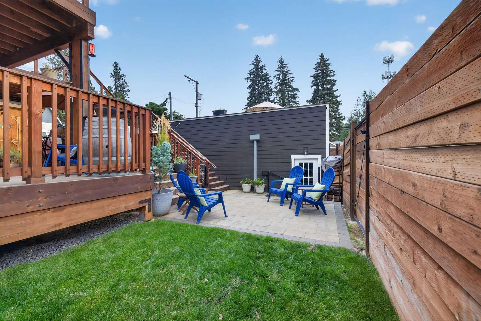 Patio with blue Adirondack chairs, potted plants, stone pavers, and a wood privacy fence.