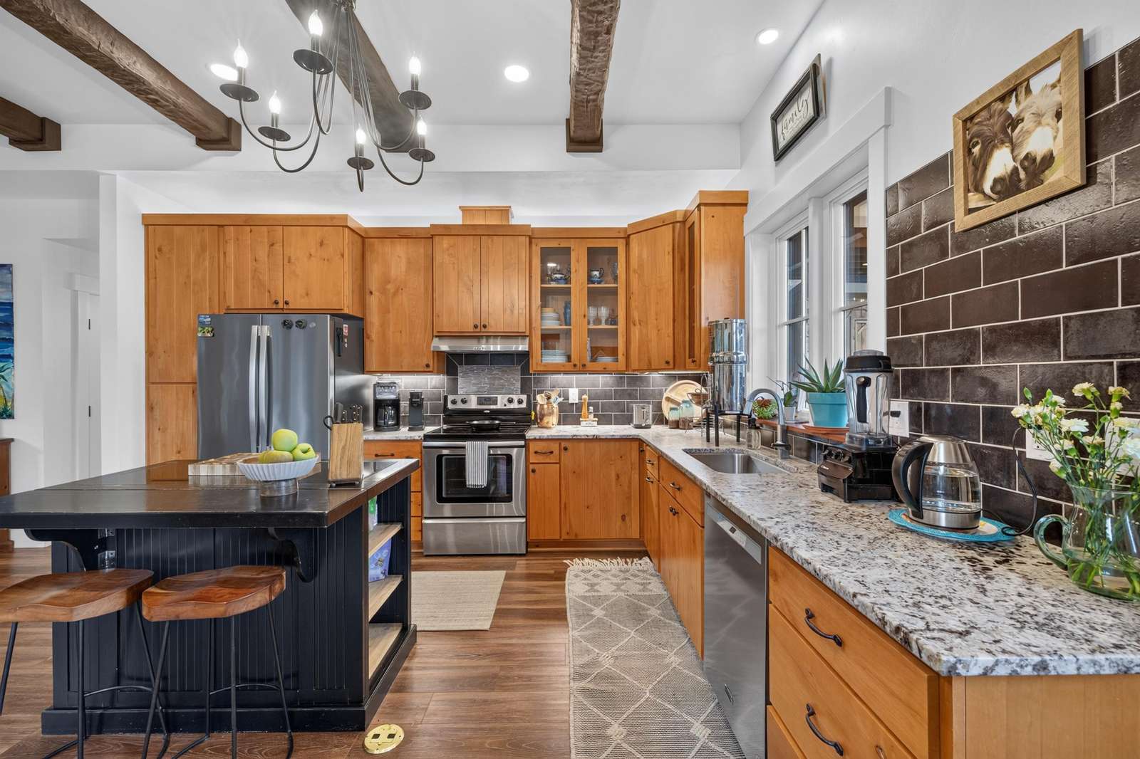 Kitchen features natural wood cabinets, granite countertops, black subway tile backsplash, and a black island with wooden bar stools.