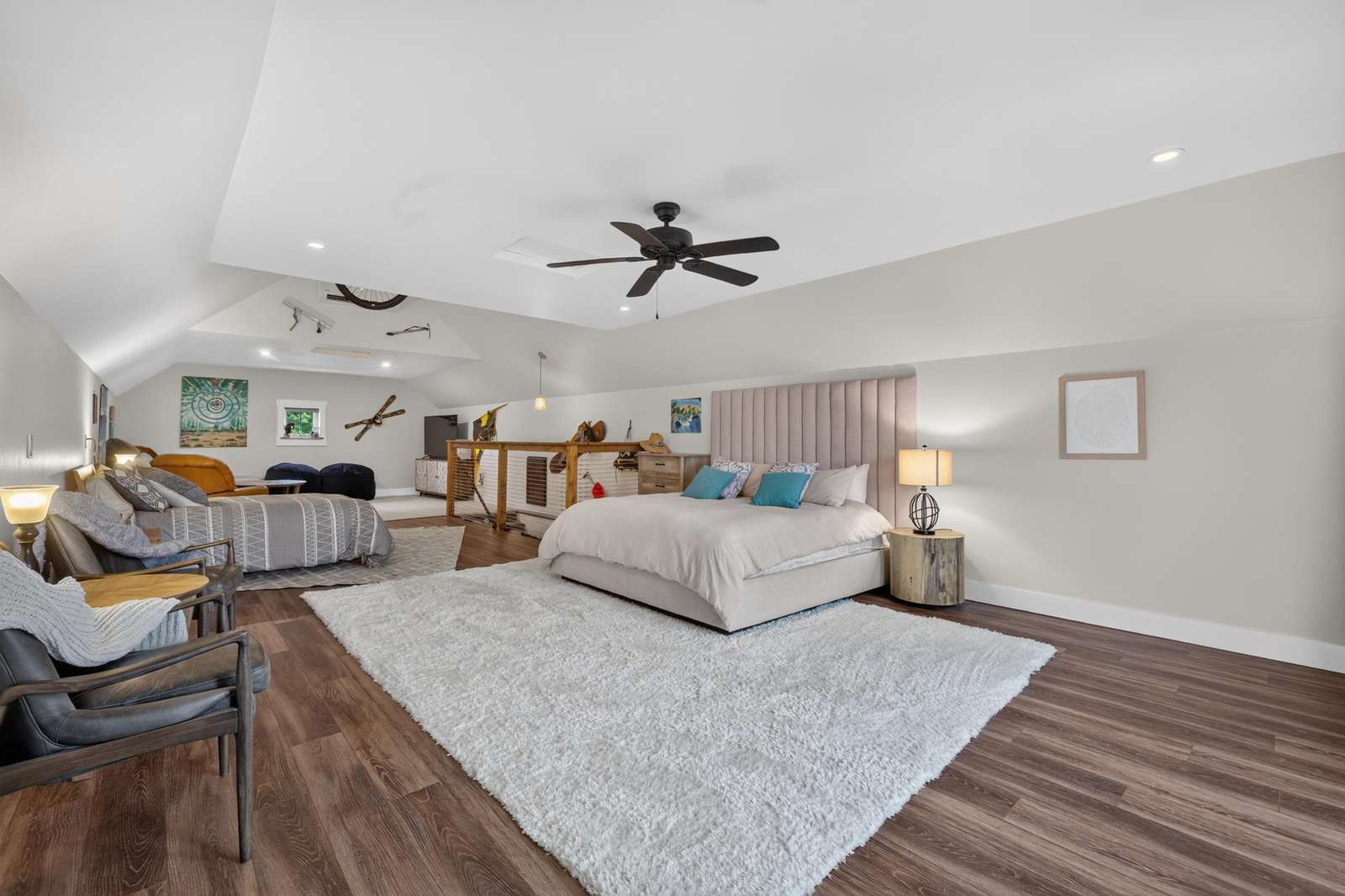Loft bedroom featuring two beds, a plush white rug, hardwood floors, and a ceiling fan overhead.