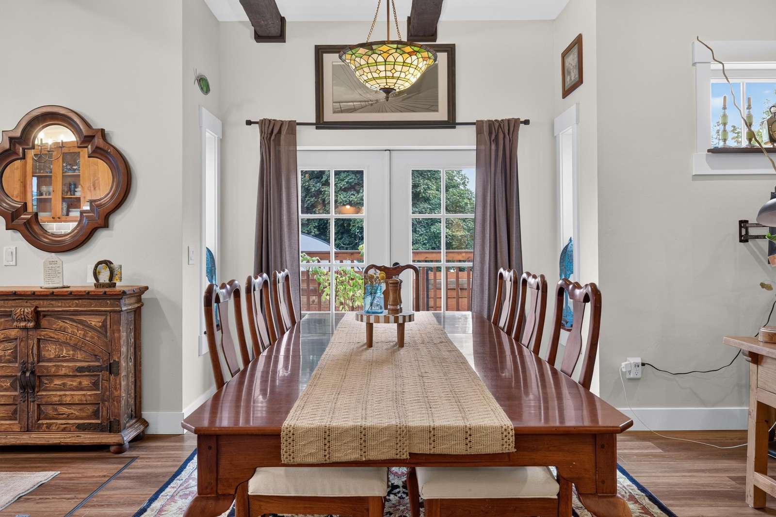 Long wooden dining table with eight chairs, beige runner, and stained glass pendant light above.