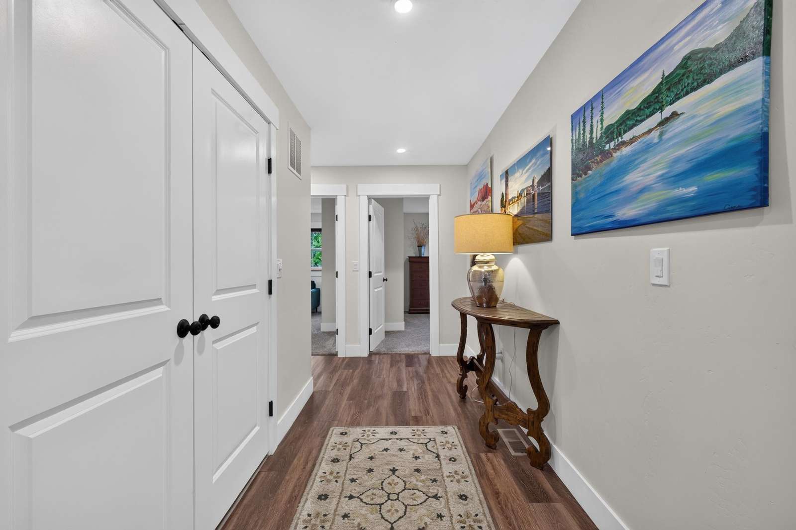Hallway with warm wood flooring, white trim doors, a patterned runner rug, and a wooden console table with lamp.