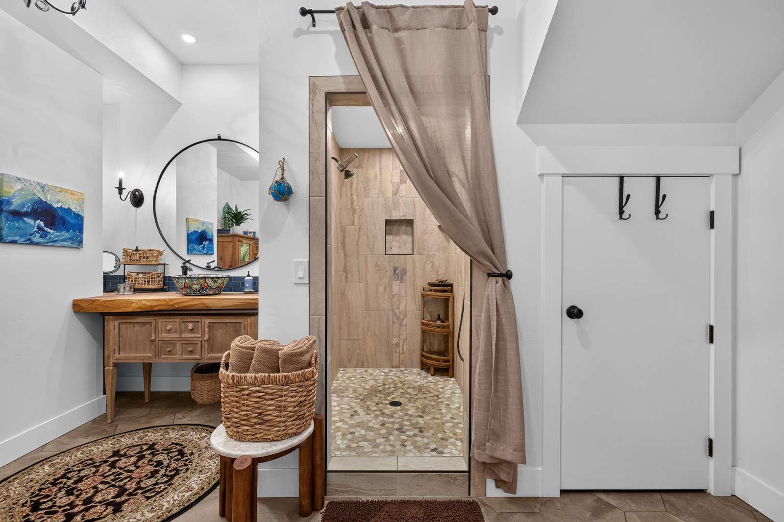 Walk-in shower features pebble tile flooring and beige stone walls with a linen curtain entry.