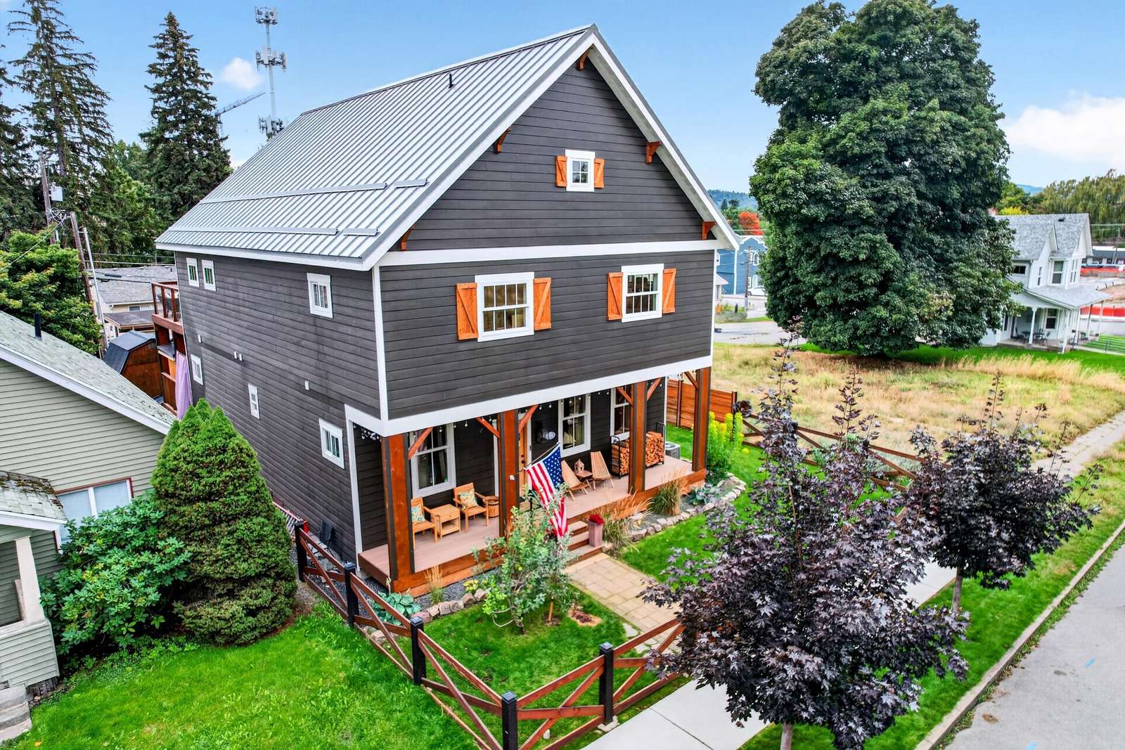 Dark gray siding with white trim and orange shutters frames the three-story house with a covered porch and wooden fence.