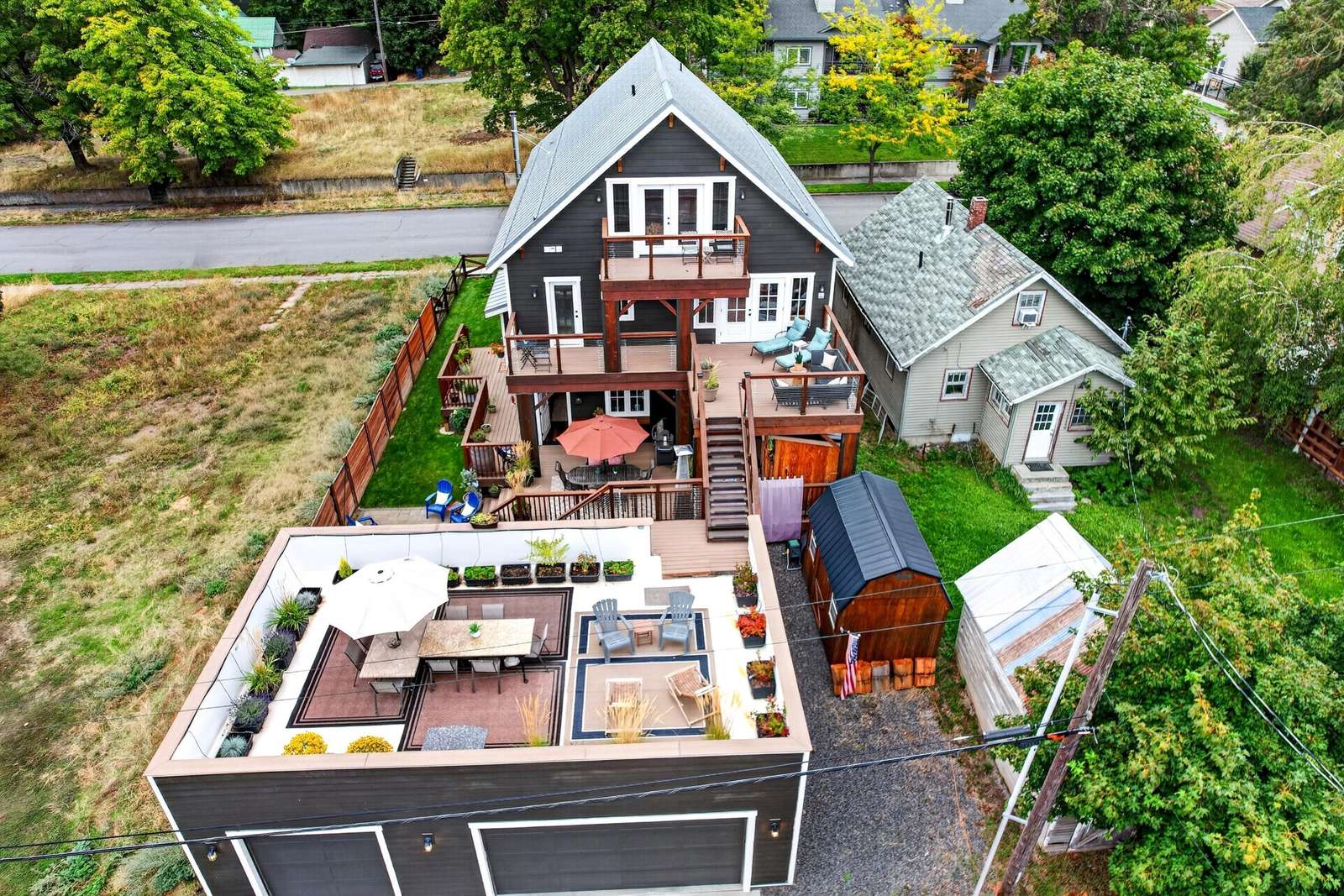 Multi-level deck with lounge chairs and umbrella-covered dining table, next to rooftop patio with seating and plants.
