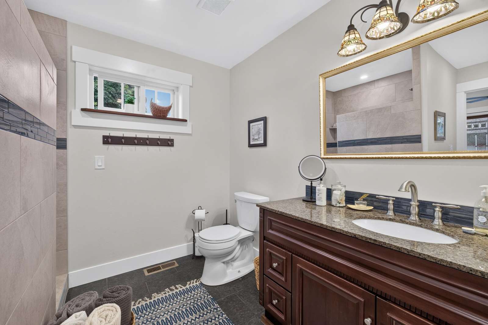 Bathroom with dark granite countertop, wood vanity, large gold-framed mirror, and tiled walk-in shower.