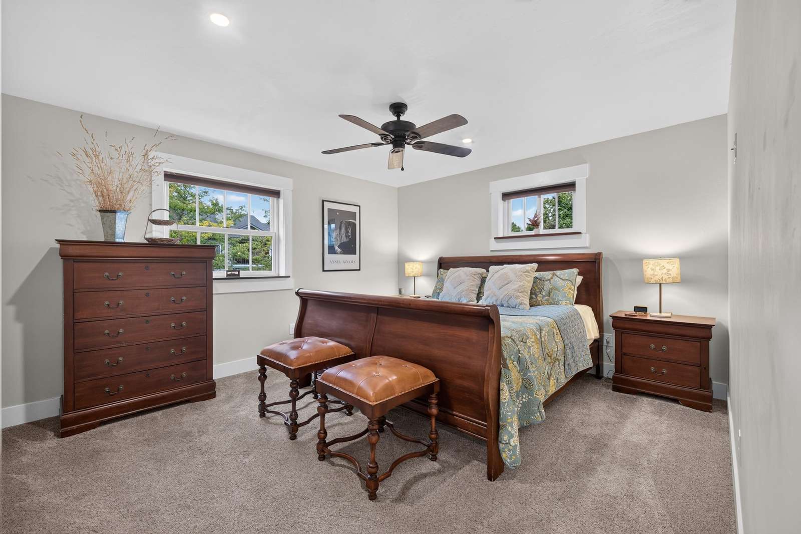 Bedroom with dark wood sleigh bed, matching dresser and nightstand, and two leather-tufted stools.