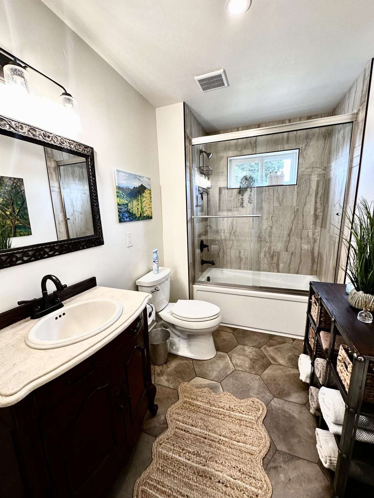 Bathroom with hexagonal tile floor, dark wood vanity, glass-enclosed tub, and a small window above the shower.