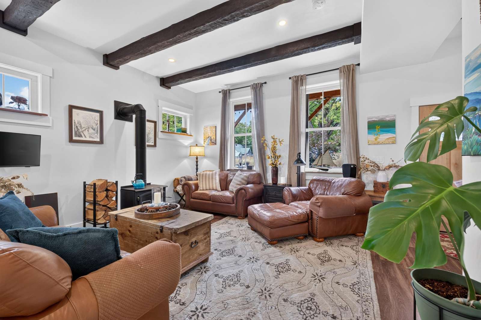 Brown leather sofas and a matching ottoman sit on a patterned rug beneath exposed dark wood ceiling beams.