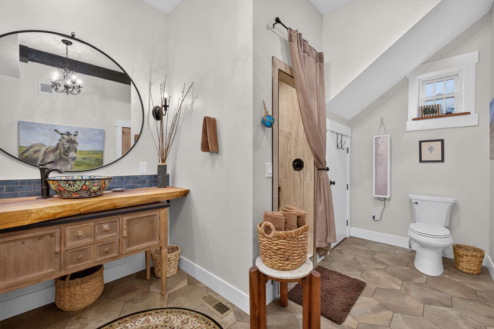 Bathroom with hexagonal tile floor, wooden vanity topped by a decorative vessel sink, and round mirror.