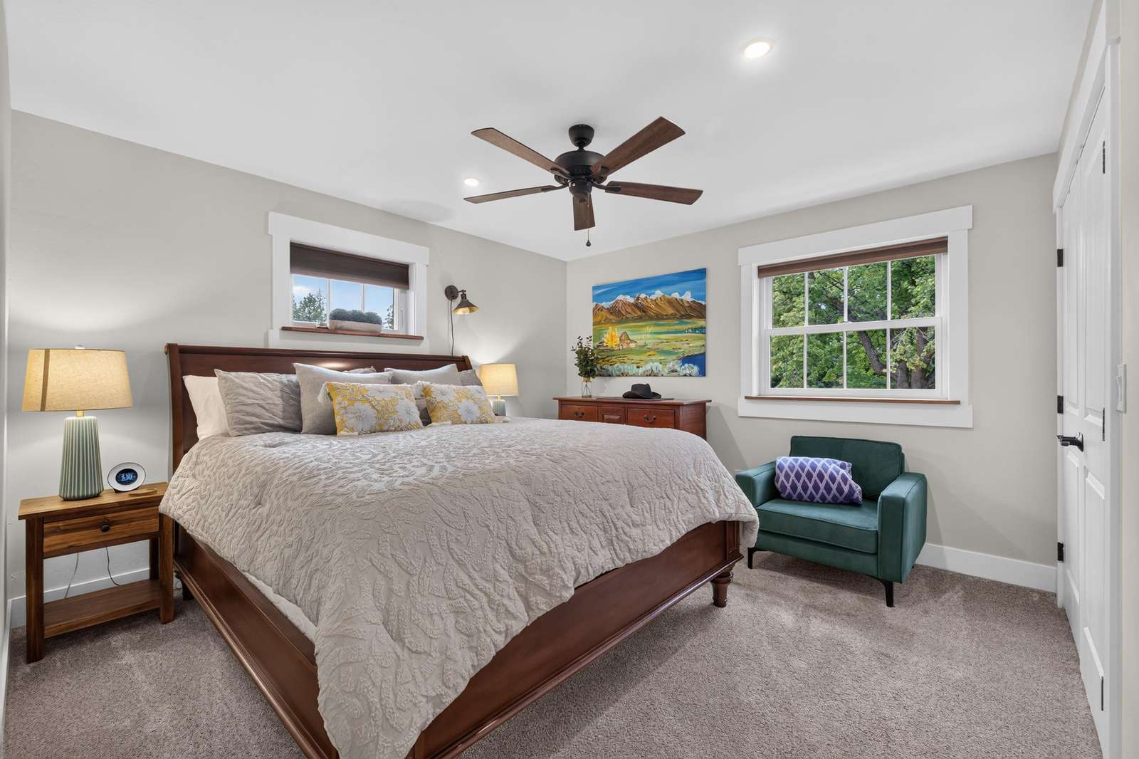 Bedroom with dark wood sleigh bed, textured white quilt, green armchair, and landscape painting above dresser.