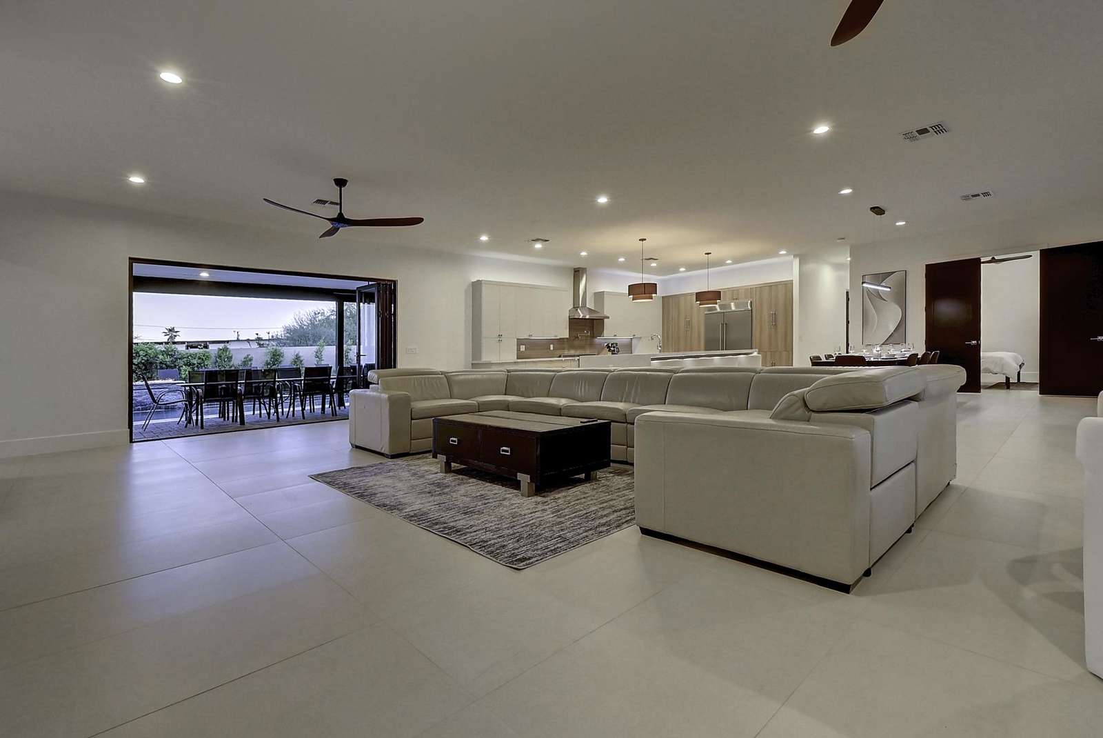 Open-plan living area with a large cream sectional on a textured gray rug and ceiling fan overhead. - property