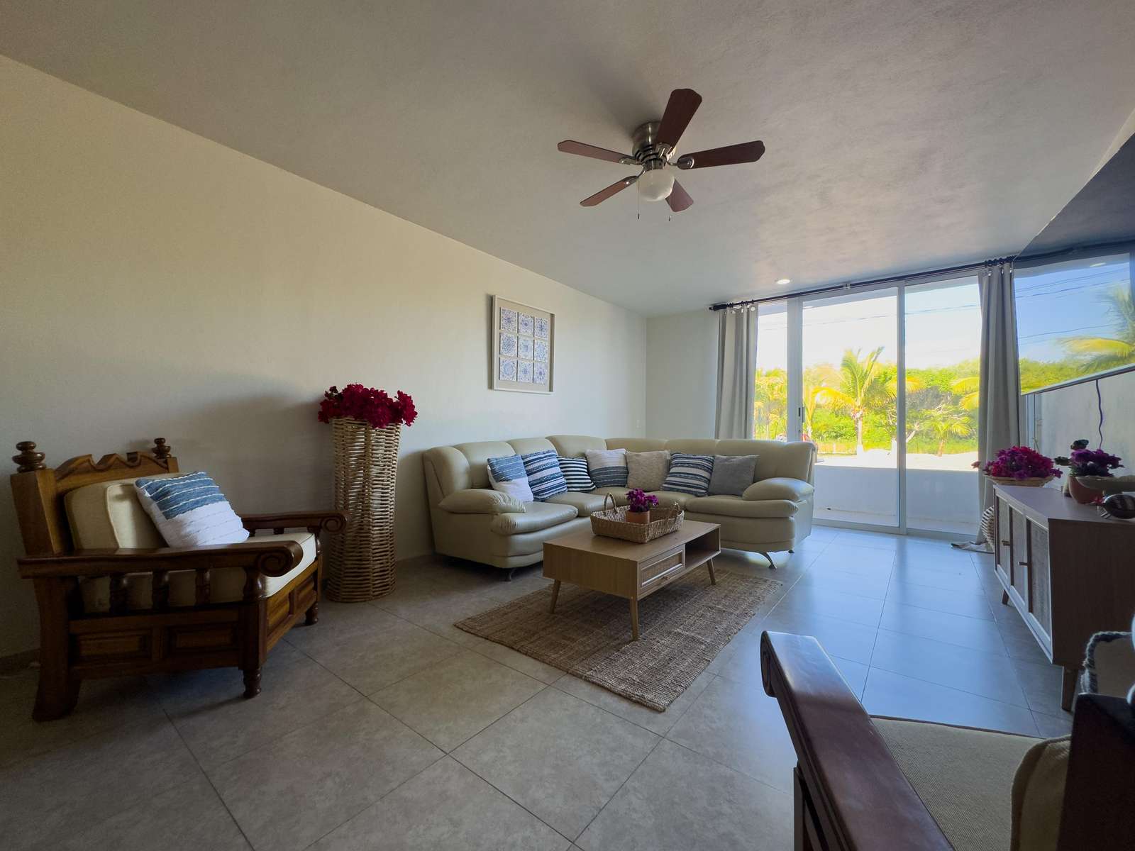 Living room with cream leather sectional, wooden armchairs, woven rug, and sliding glass door to balcony. - property