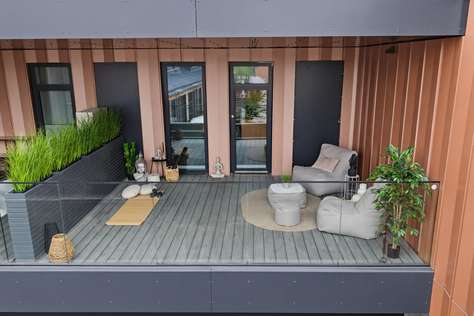 Spacious terrace with gray wood decking, glass railing, cushioned lounge chairs, and tall planter boxes with greenery.