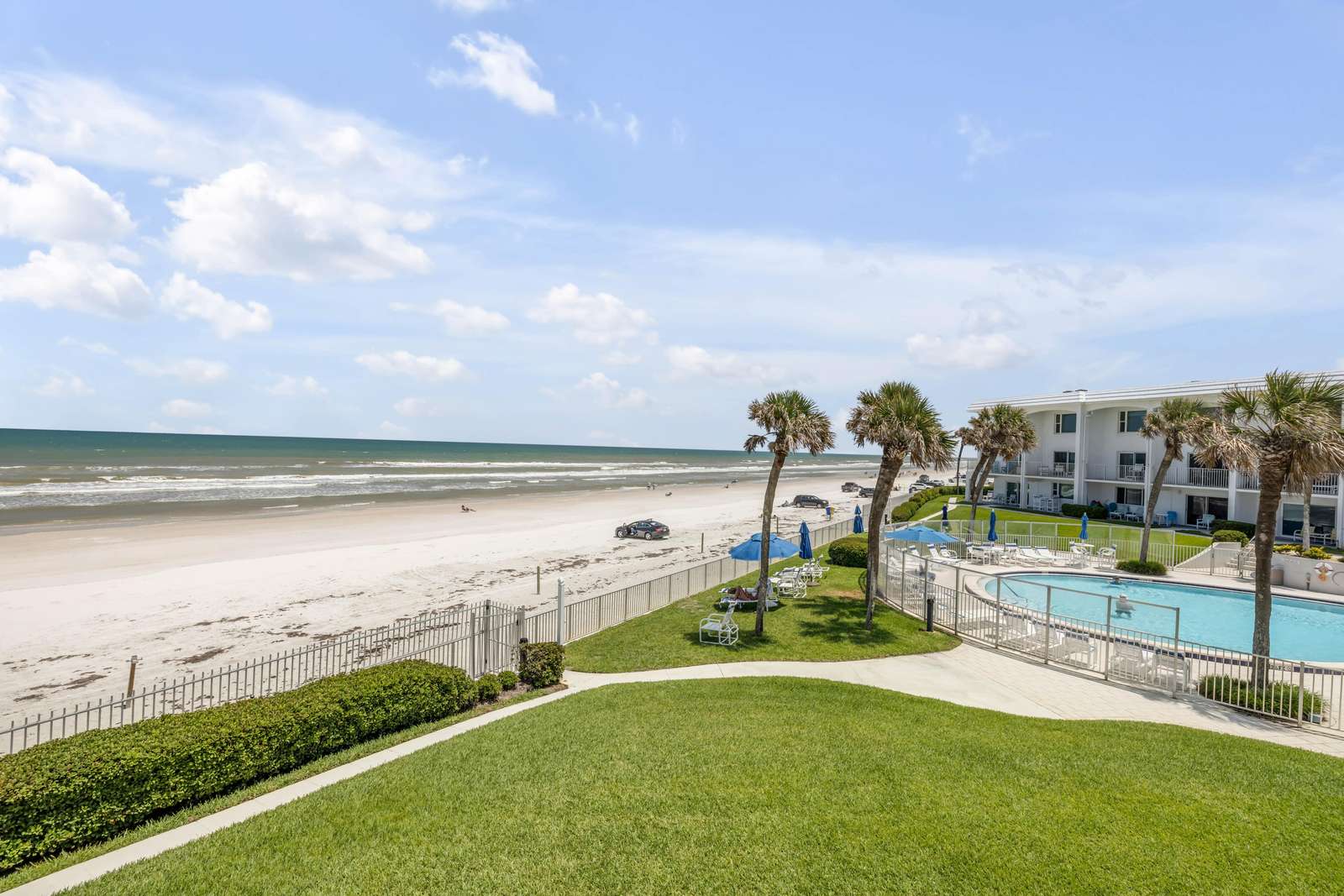 Oceanfront pool and beach access with lush green lawn - property