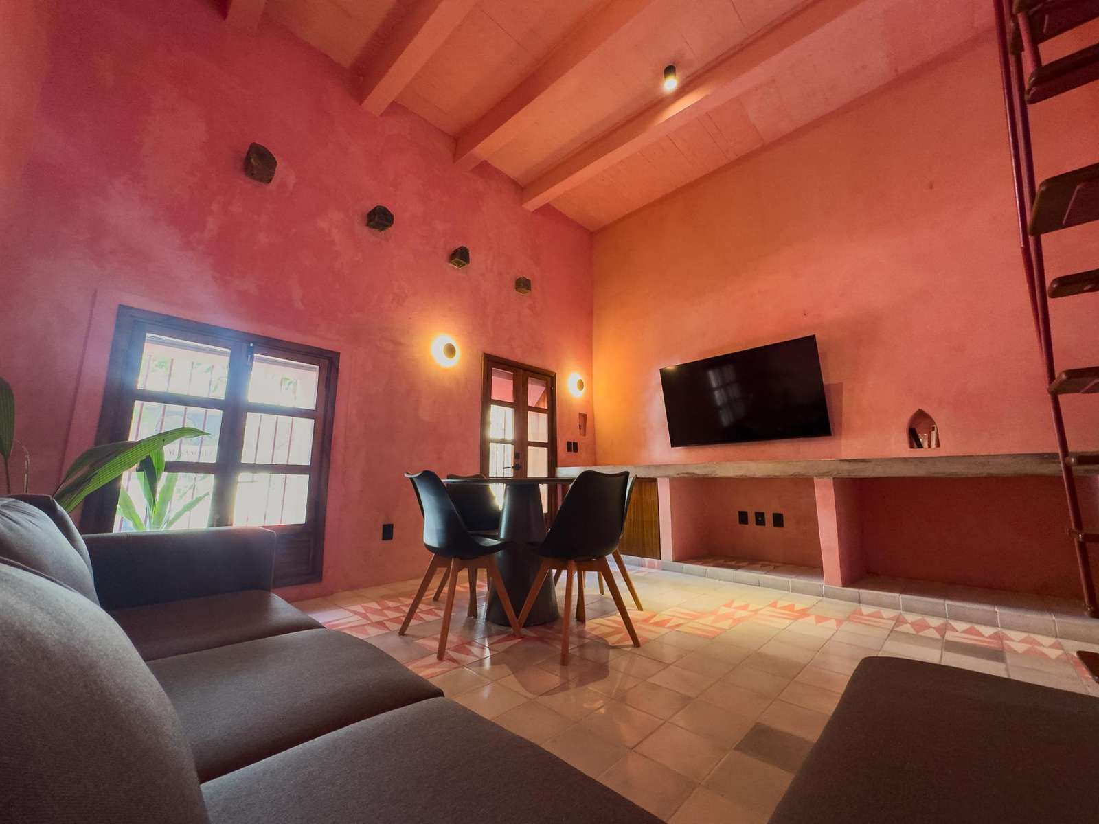Living room with textured pink walls, patterned tile floor, black dining chairs, and wall-mounted TV. - property