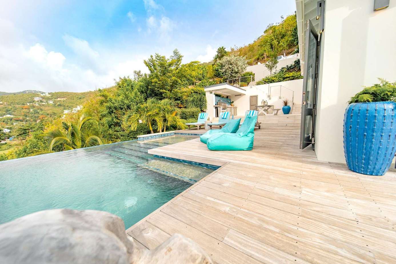 Sun-soaked poolside deck with Long Bay hillside behind and the beach directly in front