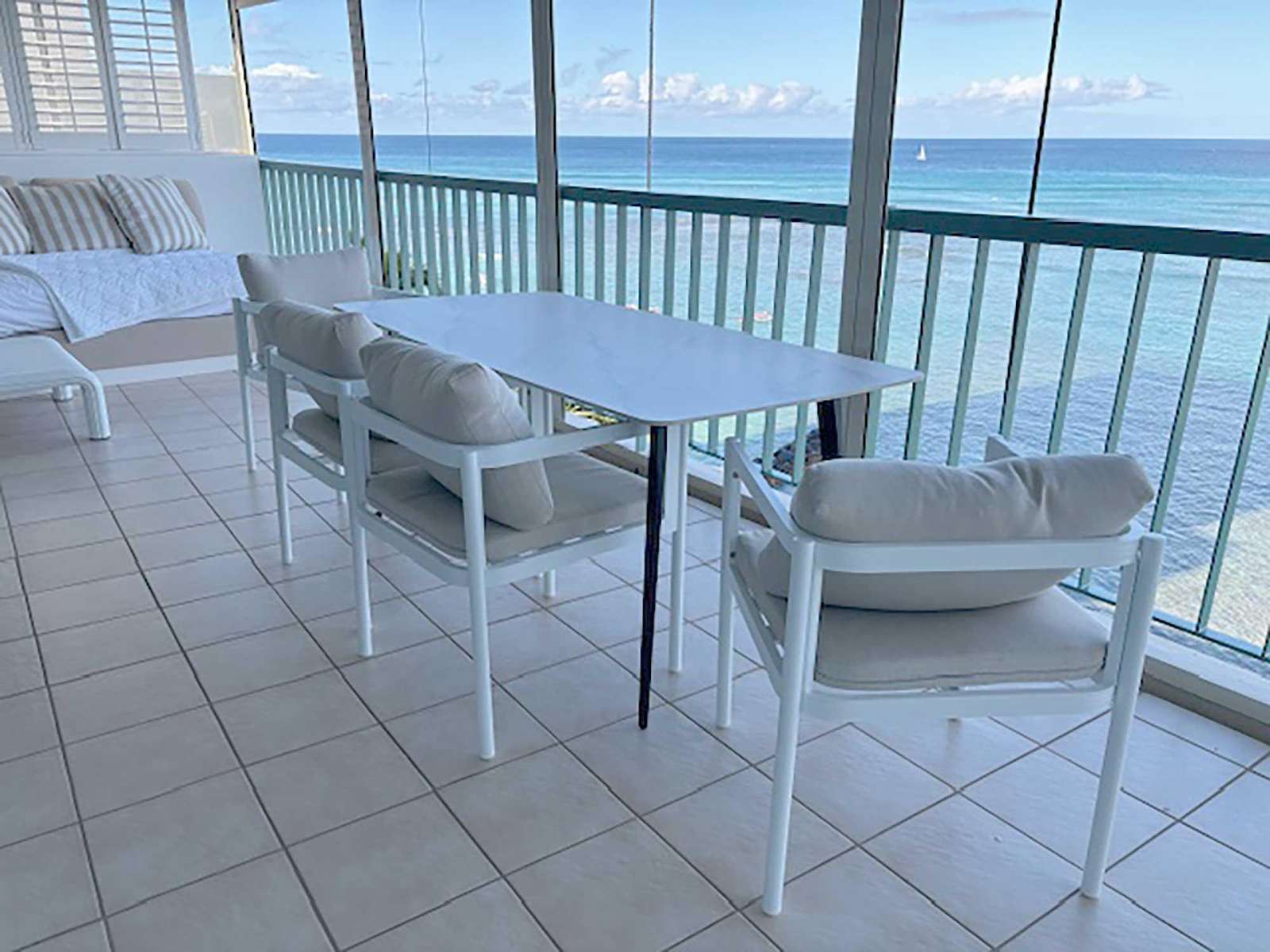 Balcony seating with cushioned white chairs and a sleek rectangular table overlooks the blue ocean and sailboats. - property