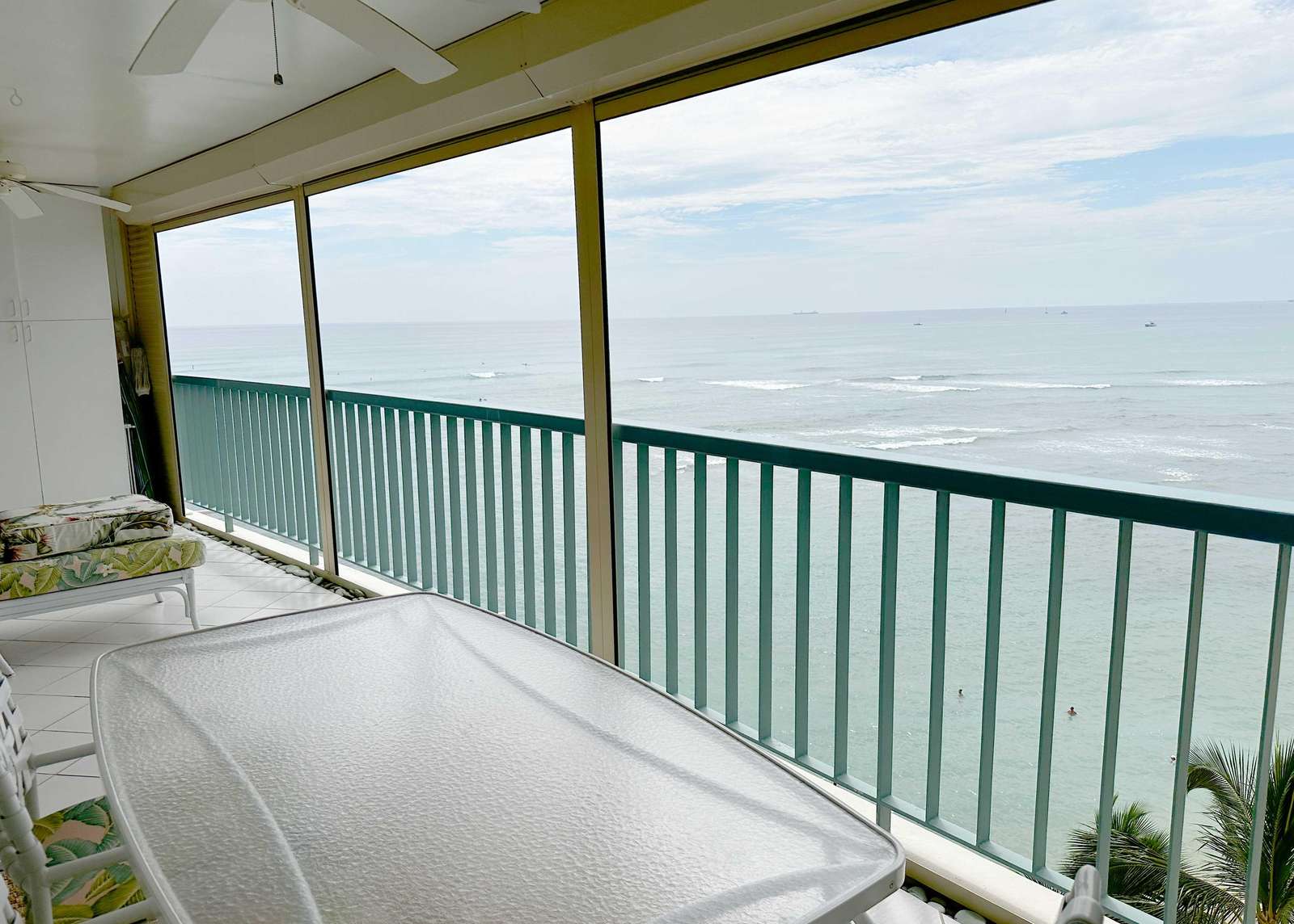 Screened balcony with tropical floral cushions on lounge chairs, white tiled floors, and ocean views. - property