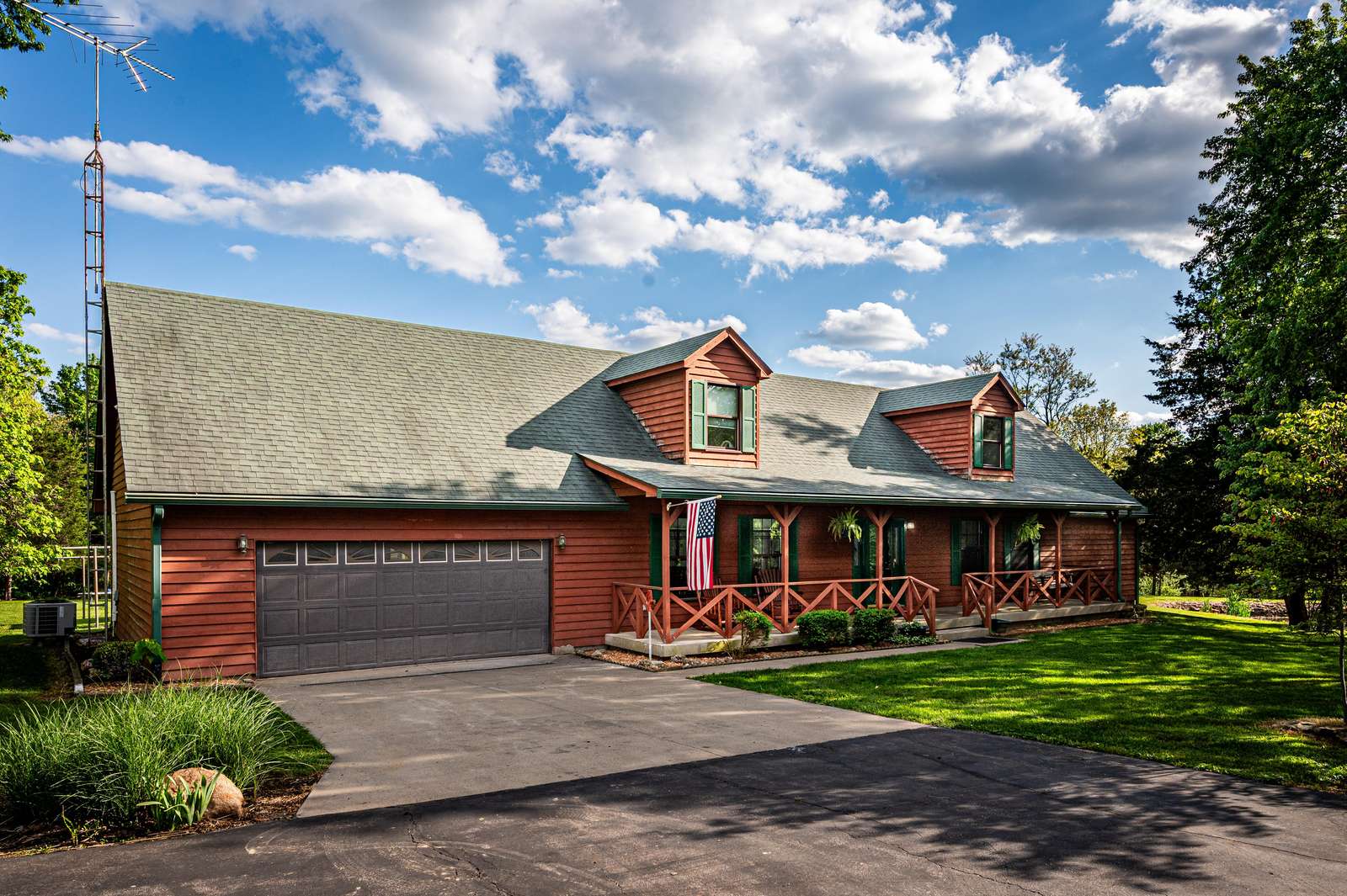 Exterior view of a red wooden cabin with green roof, dormer windows, and a two-car garage under a partly cloudy sky. - property