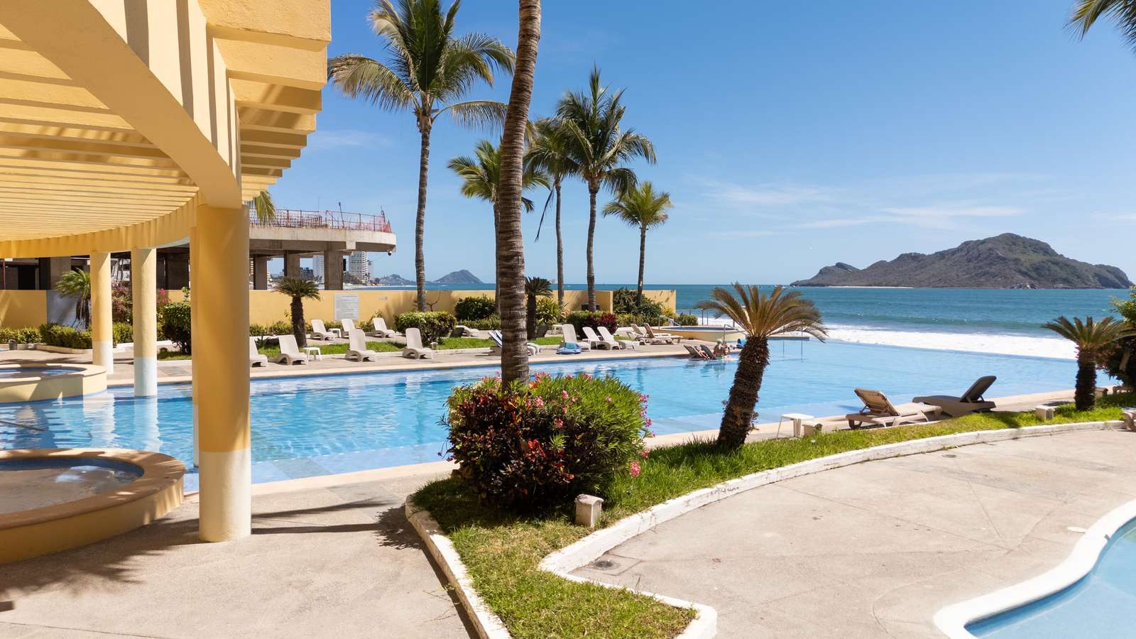 Curved yellow columns frame the blue pool beside palm trees and green shrubbery with ocean and island views. - property