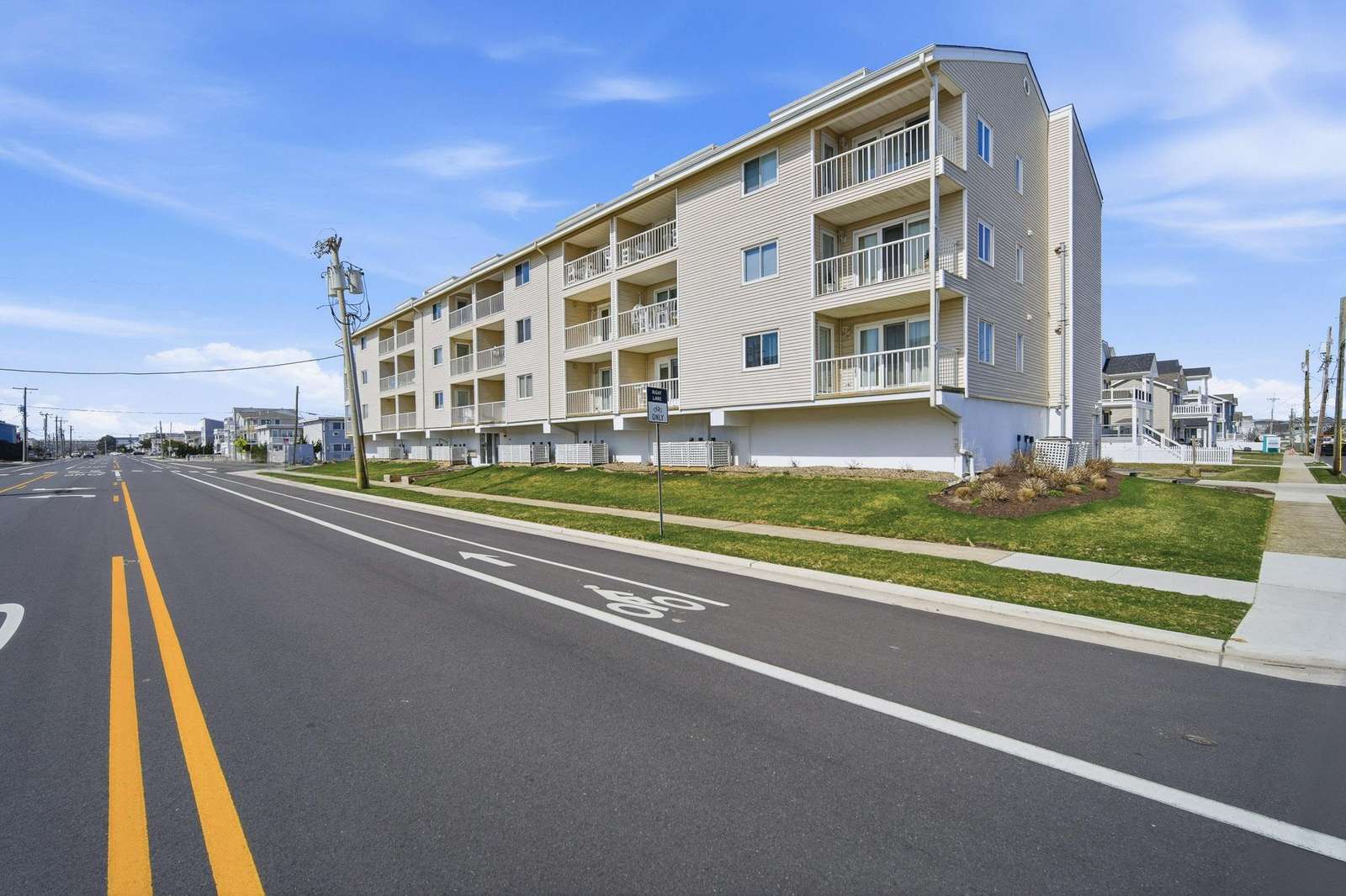 Exterior view of a beige vinyl-sided apartment building with balconies overlooking a wide street and bike lane. - property