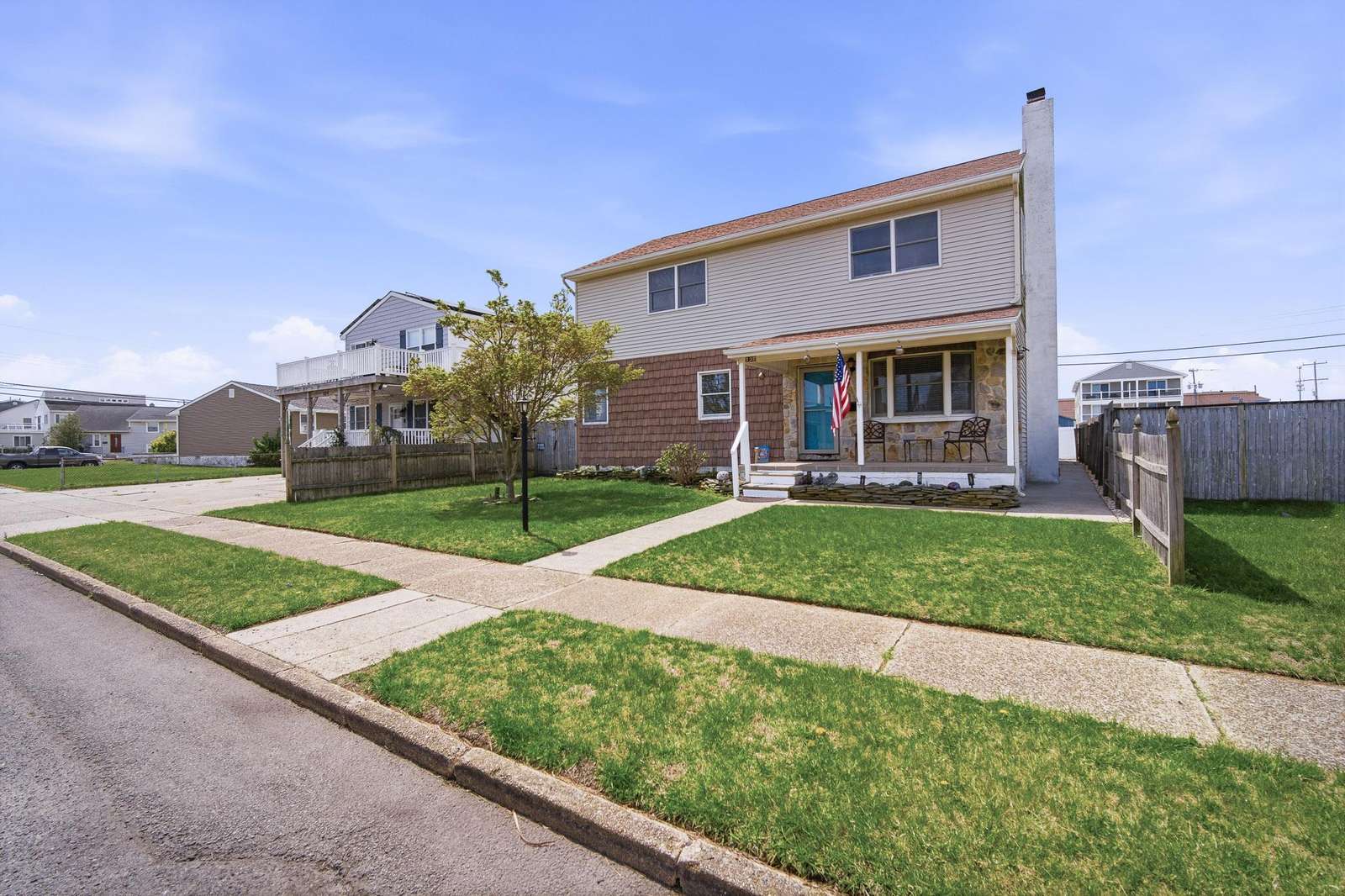 Two-story house with beige siding, stone accents, a covered porch, and a small front yard with a walkway. - property
