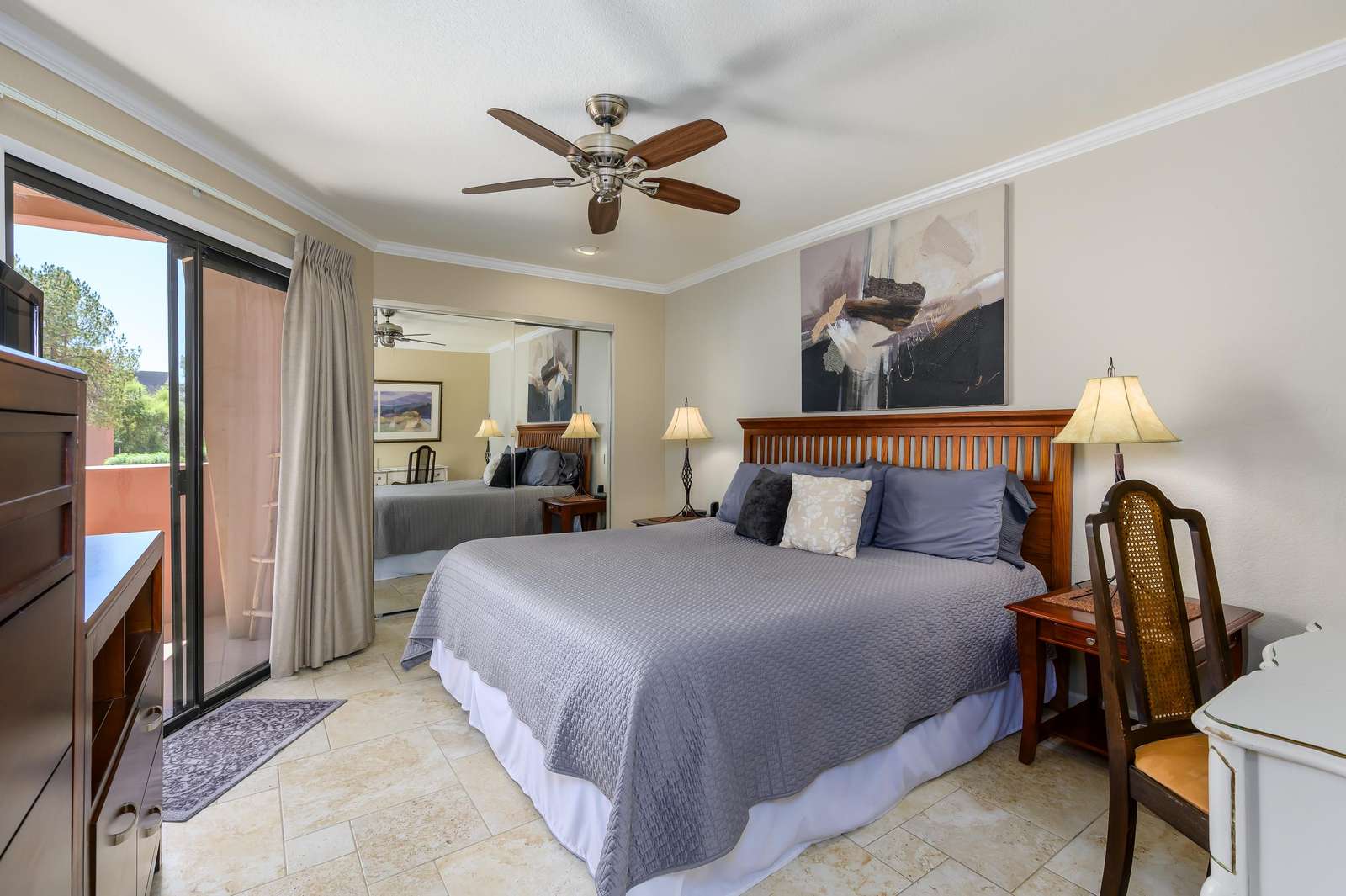 Wood headboard frames king bed with gray quilt, flanked by wooden nightstands and lamps under abstract art. - property