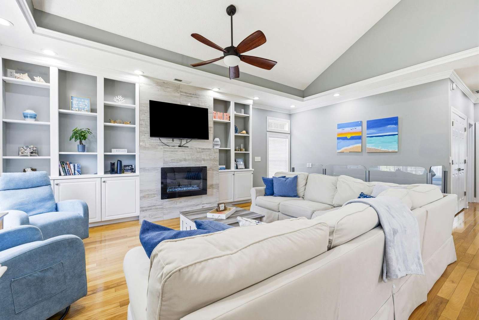 Vaulted ceiling with dark wood fan crowns the living room featuring white built-ins, a mounted TV, and a gas fireplace. - property